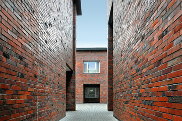 Narrow alley between two red brick walls in perspective.