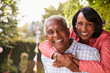 © Monkey Business - Senior black couple piggyback in garden looking at camera