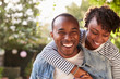 © Monkey Business - Laughing young black couple piggyback in garden, to camera