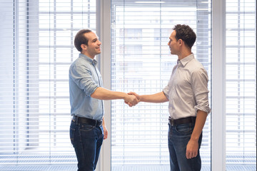 Wall Mural - Two colleagues dressed casually shaking hands in modern office interior