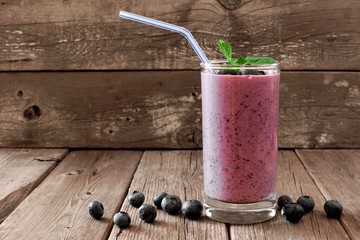 Wall Mural - healthy blueberry smoothie in a glass with berries, mint and straw against a rustic wooden backgroun