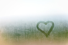 Abstract Blurred Love Heart Symbol Drawn By Hand On The Wet Frozen Window Glass With Sunlight Background.