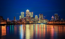 Canary Wharf Business District In London At Night Over Thames River.