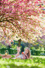 Beautiful young woman having picnic in blooming spring park