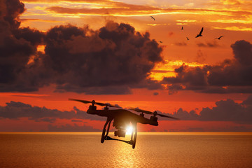 Wall Mural - silhouette of flying drone in glowing red sunset sky above sea