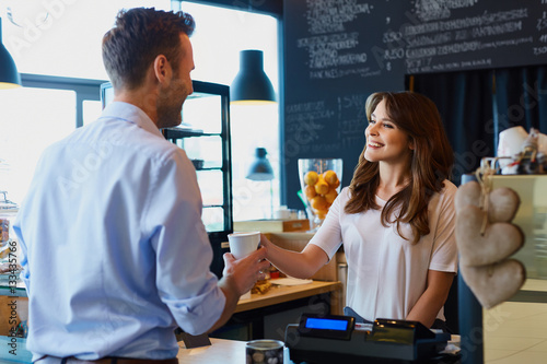 Fotografie, Obraz Young female barista serving coffee to customer in cafe