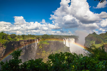 Wall Mural - Victoria Falls from the side.  A rainbow and blue sky with clouds on a sunny day