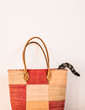 Colorful straw bag with cat's tail jutting out of it - white background, vertical.