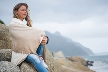 Thoughtful Woman Wrapped In Shawl Sitting On Rocks