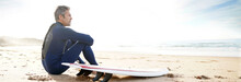 Surfer Sitting On Sandy Beach, Next To Surfboard