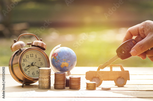 Fotografía hand holding key of car with pile of money, alarm clock and globe on table, conc