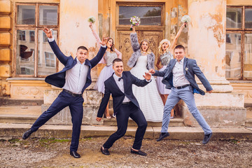 Wall Mural - bride and groom with bridesmaids and groomsman near old castle with columns jumping and embracing together.