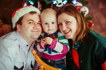 The mother,father and son sitting near Christmas tree