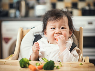 Wall Mural - baby girl eating broccoli,carrot vegetable first time at home