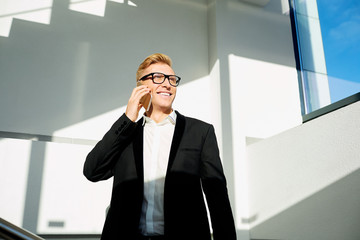 Businessman positive  blonde in a business suit, with glasses talking on phone, smiling. The sunlight  his face.