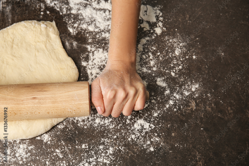 Young woman rolling out dough in kitchen