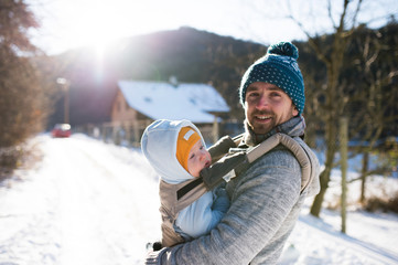 Father holding his son in baby carrier. Sunny winter nature.