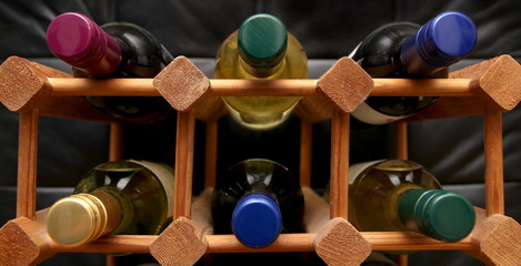 Wooden wine rack with various color bottle tops on dark backgrou