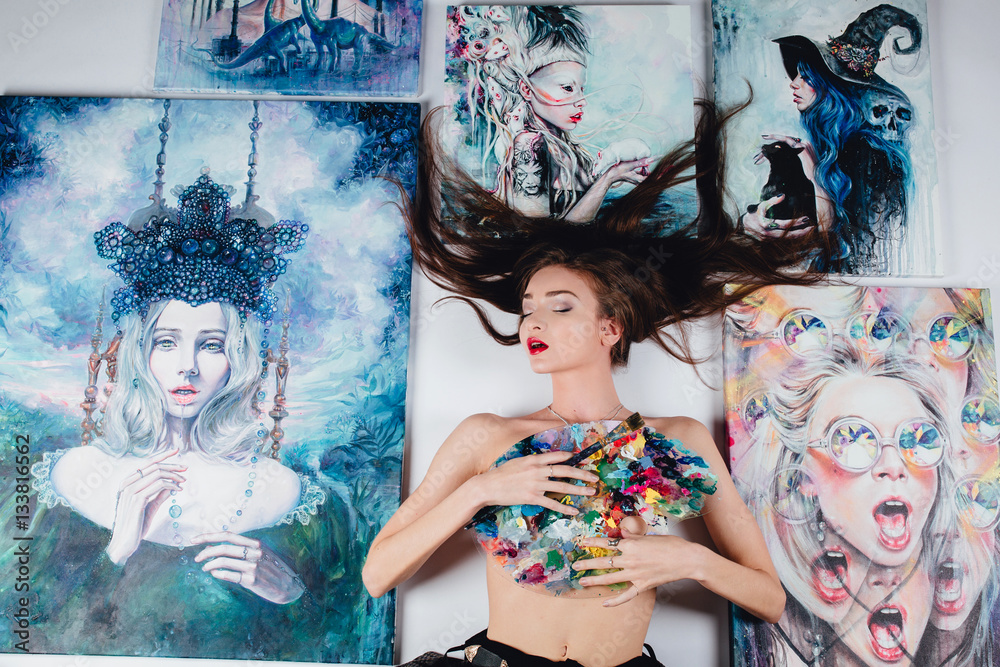 Beautiful female Nude artist surrounded by paintings canvas on the