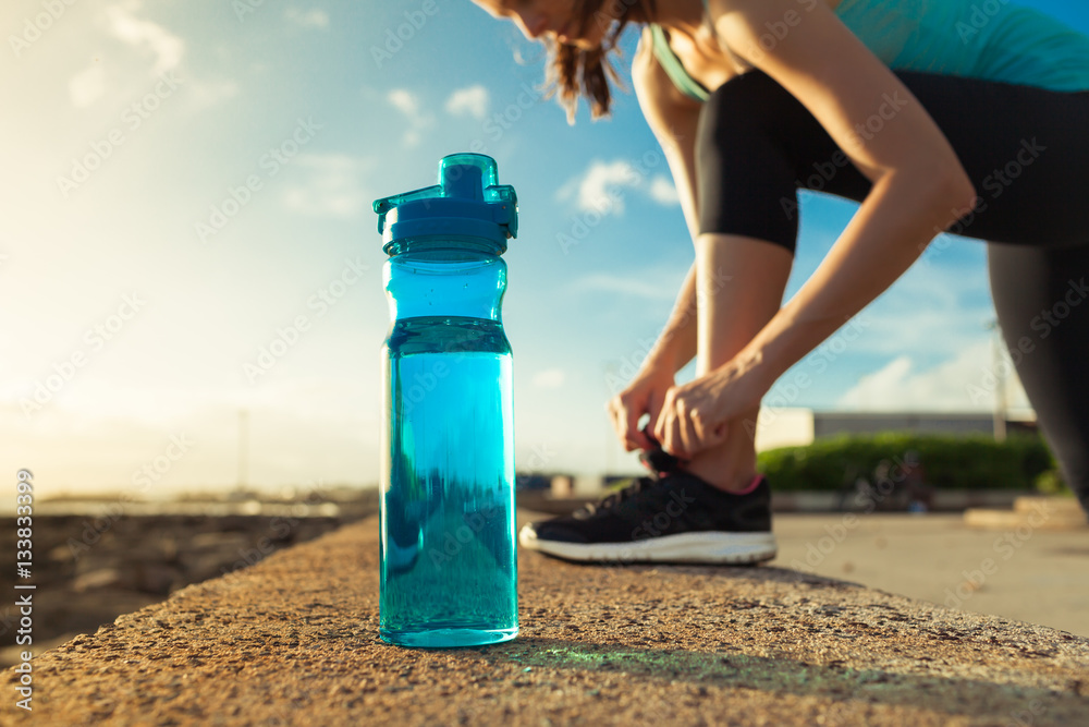 Drinking water concept. Female runner tying her shoe next to bottle of water. - obrazy, fototapety, plakaty 