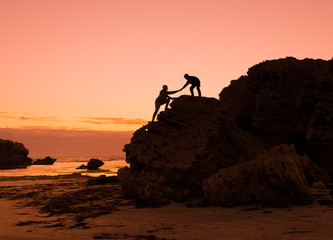 Two people climbing up the cliff teamwork help to succsess