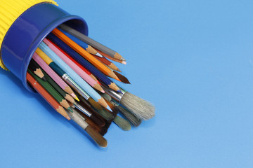 Color pencils and paintbrush box on blue table.