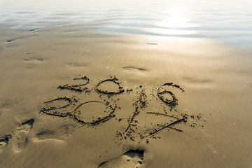 New year 2017 written on seashore sand at sunrise.