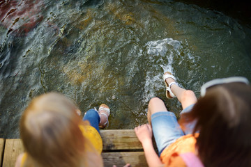 Wall Mural - Two cute little girls sitting on a wooden platform by the river or lake