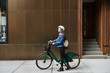 © Cavan Images - Young woman walking with bicycle on sidewalk by building