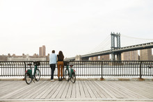 Rear Vie Of Couple Standing With Bicycles On Footpath By Manhattan Bridge