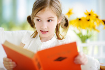 Adorable little girl reading a book in white living room