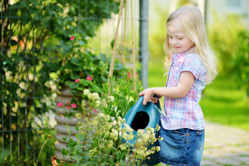 Wall Mural - Cute little girl watering flowers in the garden