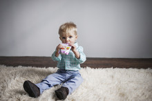 Portrait Of Cute Baby Boy Drinking Juice From Package While Sitting On Rug At Home