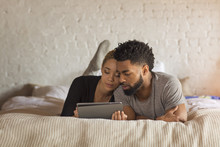 Couple Using Tablet Computer While Relaxing On Bed