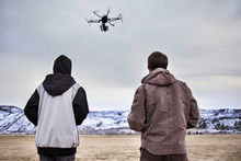 Rear View Of Father And Son Flying Drone Over Field