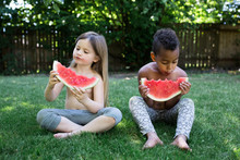 Children Eating Watermelon Slices While Sitting On The Grass