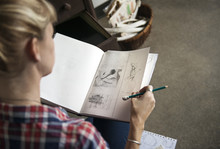 Female Artist Looking At Sketches In Book While Sitting At Home