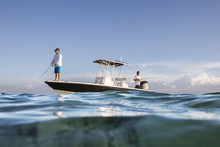 Low Angle View Of Men Fishing While Standing On Boat At Sea Against Sky
