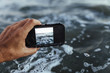 © Cavan Images - Close up of hand taking photograph of the sea with a smartphone