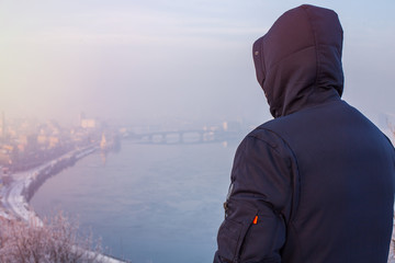 Hipster man traveler in hood looking at winter city landscape