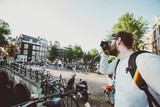 Fototapeta  - Tourist photographer takes selfie photo in Amsterdam, Netherlands. Tourist walks near canals on excursion and take photos for his blog.