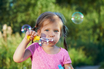 The girl in the pink dress 3 years and two braids enjoys life, inflating bubbles.