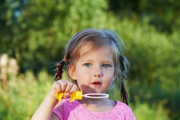 The girl in the pink dress 3 years and two braids enjoys life, inflating bubbles.