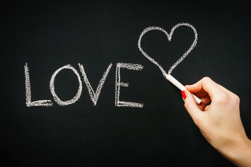 woman's hand writing on the blackboard the word love