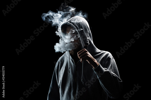 Fotografía One man in the hood vaping e-cigarette and blowing a cloud.