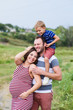 © o_lypa - Pregnant family of three in expectation of baby. Father mother and son playing together in day outside. Happy people hugging. Smiling laughing baby sitting on shoulders of daddy.