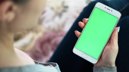 Wall Mural - Beautiful girl holding a smartphone in the hands of a green screen green screen, hand of man holding mobile smart phone with chroma key green screen on white background, new technology concept