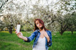 © anna_gorbenko - Young pretty smiling caucasian woman in jeans jacket and white dress taking selfie near blooming spring tree. Youth, freshness, beauty, happiness concept.