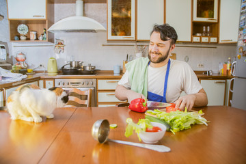 Wall Mural - a man cooks in the kitchen beside him sits a funny beautiful cat