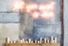 Neon Inscription "All You Need Is Love" On A Grey Concrete Wall And Many Candles Under Them